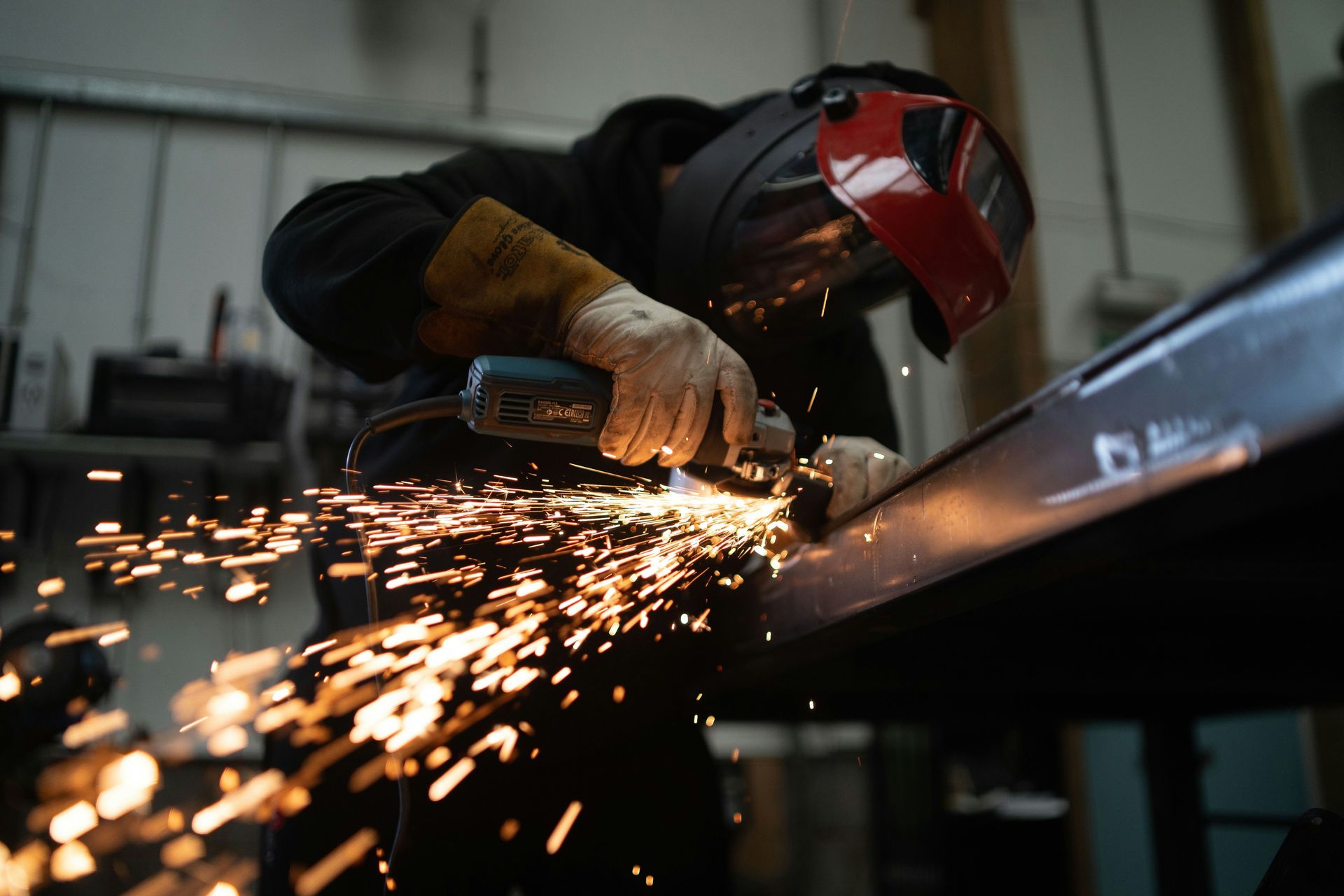 A person wearing a welding helmet grinding a metal beam with sparks flying