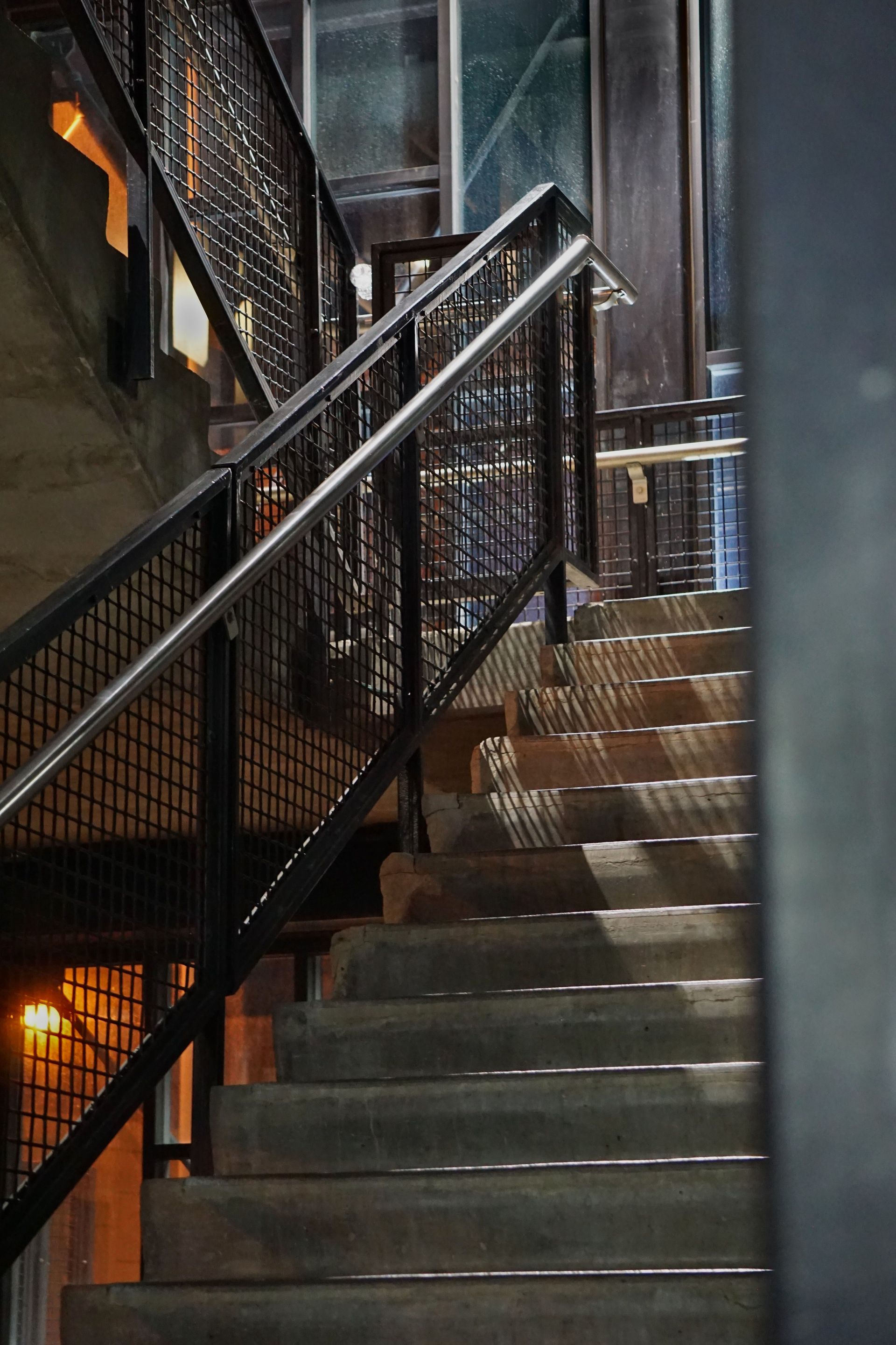 Vertical shot of industrial stairs with a metal handrail casting shadows.